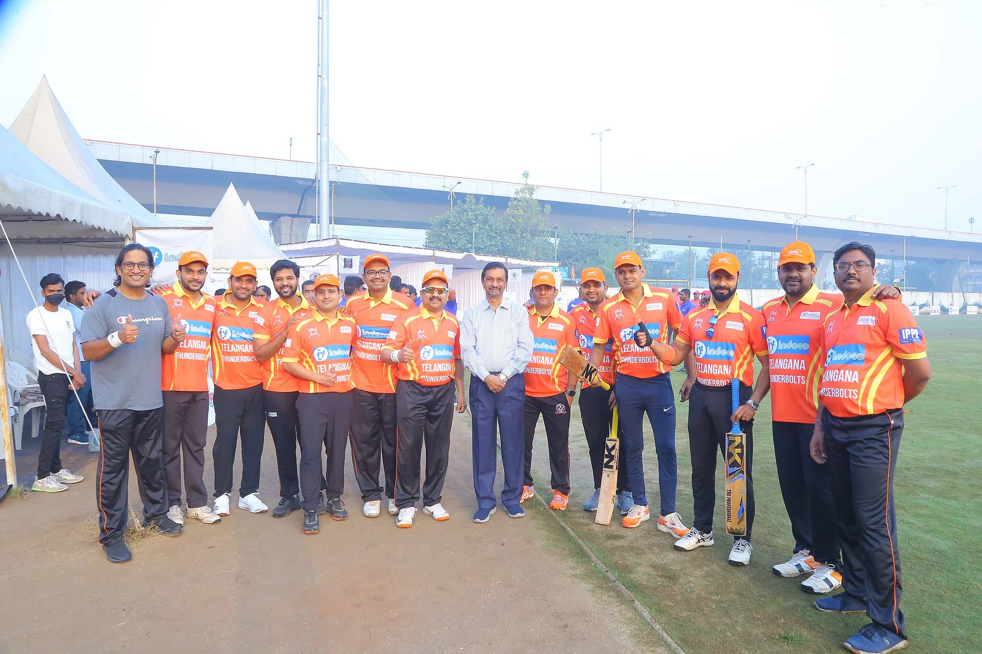 A pediatricians' cricket team in orange jerseys lined up with bats on the outfield