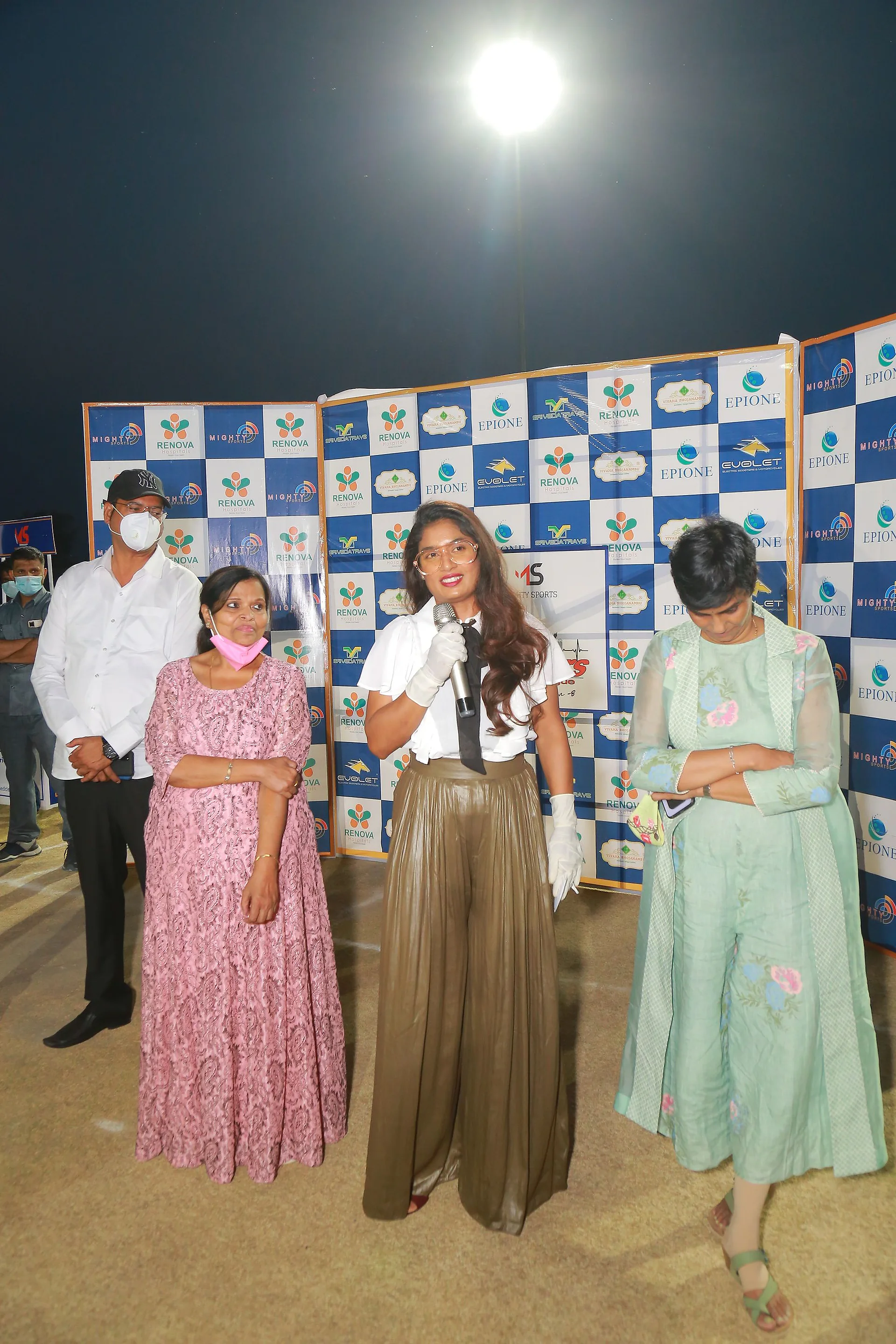 Guests being felicitated in front of the sponsor backdrop at a night match