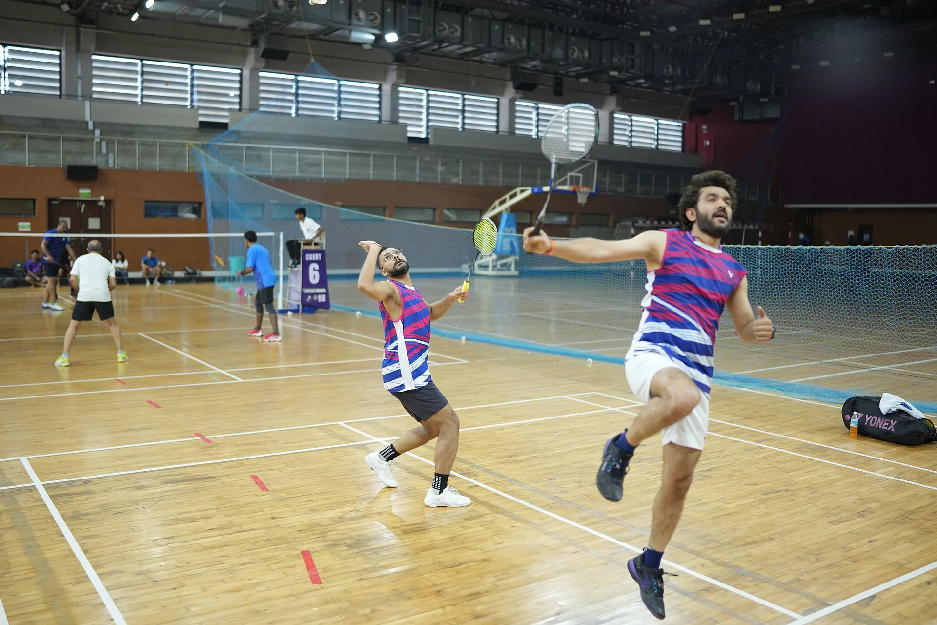 Two doctors in mid-air during a fast doubles badminton rally at the National Doctors Badminton Championship in Goa