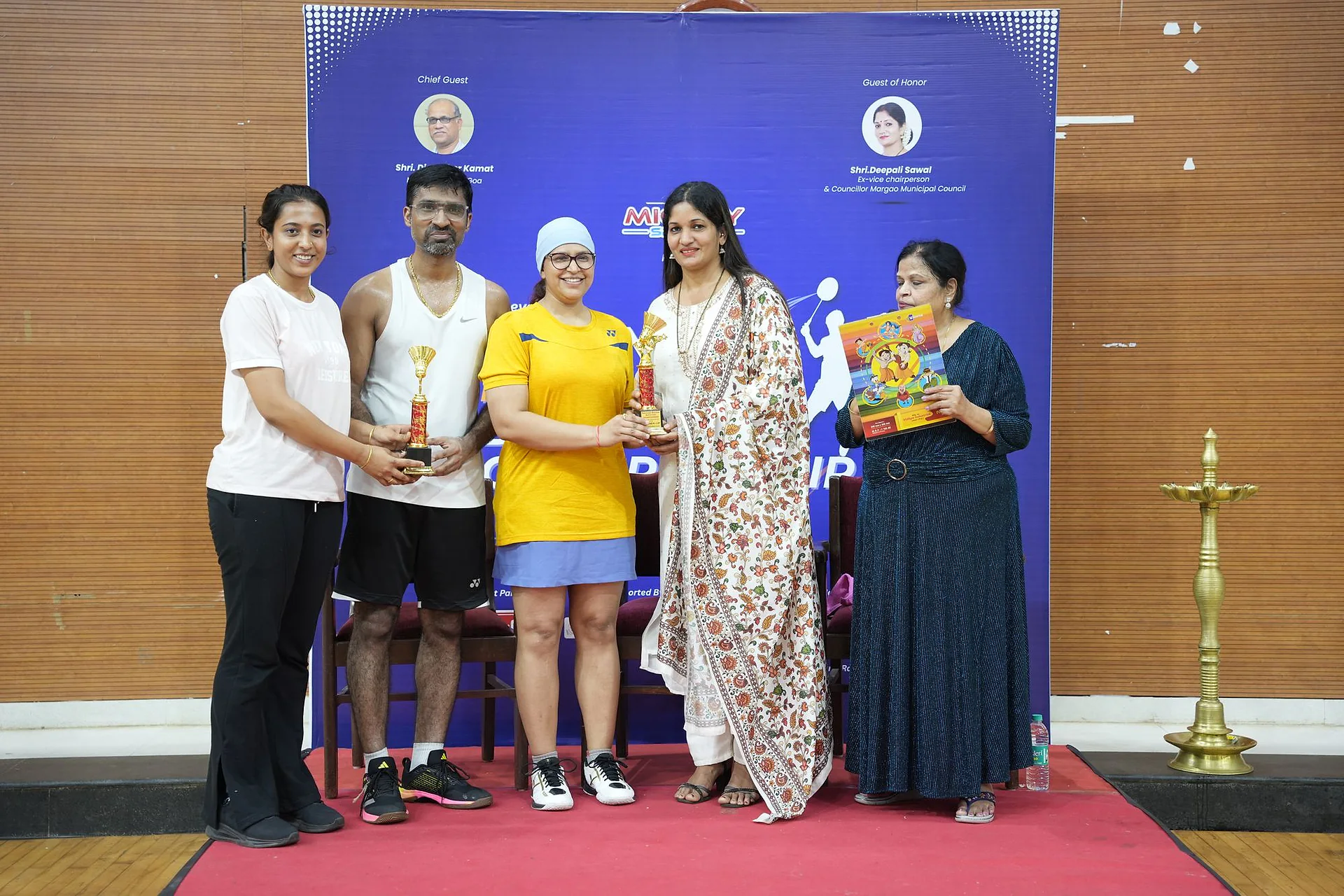 Winners holding trophies beside guests on the prize-giving stage