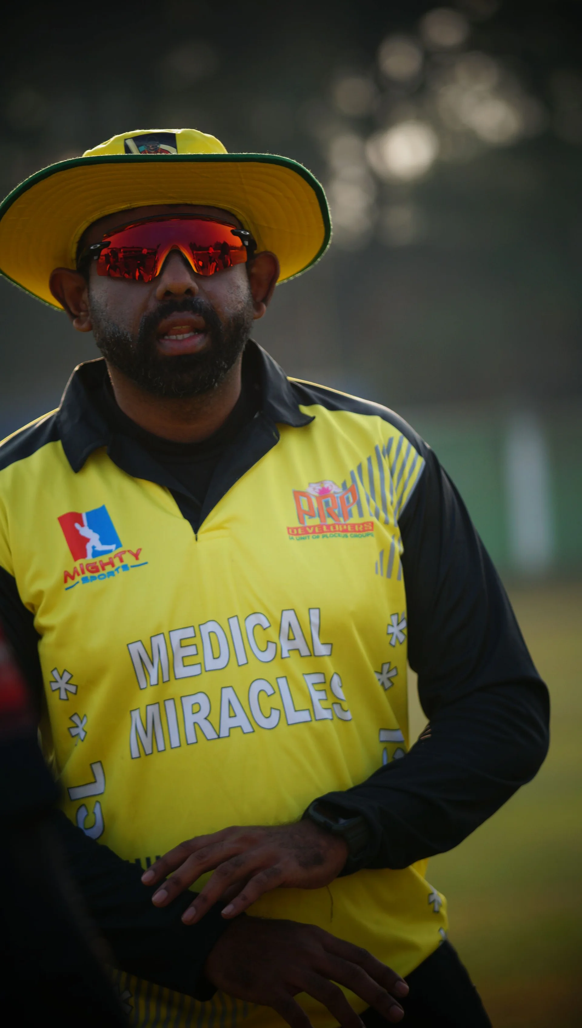 A player in a yellow Medical Miracles jersey and sunglasses at the National Doctors Cricket League